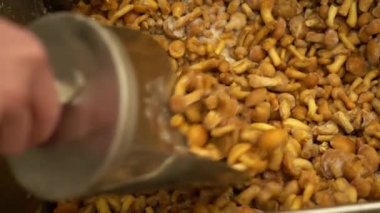 Beyaz lekeleri ile metal bir kepçe kullanan bir adam mağaza yakın tavada alttan dondurulmuş lezzetli sarı mantar gözyaşları. Piyasada birçok dondurulmuş bal agaric.