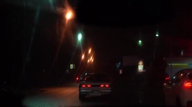 Arabanın içinden kirli ıslak cam üzerinden dışa görünümü. Araba gece yolu üzerinde bir araba akışı hareket. Işık ve araçların yansımaları.