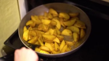 Siyah plastik pişirme çatal kullanarak beyaz bir pullover bir kadın el evde fırında bir fırın tepsisine bir ızgara baharat ile kızarmış patates lezzetli dilimleri karıştırır. Duman buharlaşır..