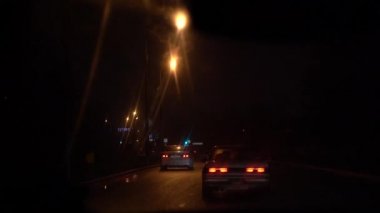 Arabanın içinden kirli ıslak bir ön camdan dışa doğru görünüm. Araba gece yolunda bir araba akışı içinde hareket eder. Işık ve araba yansımaları. Tabeladaki yazıt: Eniseyskaya caddesine dön.
