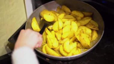 Siyah plastik pişirme çatal kullanarak beyaz pullover bir kadın el evde fırında fırın tepsisine ızgara sarı sos baharat ile kızarmış patates lezzetli dilimleri karıştırır. Duman buharlaşır..