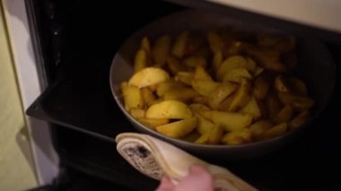 Beyaz bir bez kullanarak beyaz bir pullover ile kadın el fırına bir fırın tepsisine baharat ile kızarmış patates ızgara slaytlar, fırın kapağı kapatArak ve seçici anahtarı döner.