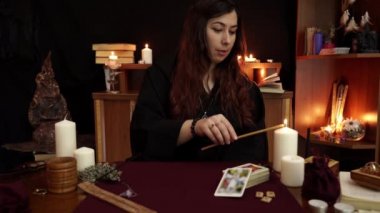 Cadı, siyah mantolu bir falcı sarı kilise mumuyla beyaz mumu yakıyor ve karanlık mistik arka planda büyülü bir ayin yapıyor. Okült, esrarengiz, kehanet ve cadı kavramı.