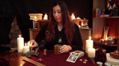 Bir cadı siyah manto lu falcı harç ezme ve havaneli kullanarak sallar pelin koymak. Büyülü bir ritüel. Tarot kartları, masada beyaz mumlar. Gizli, ezoterik, kehanet ve Wicca kavramı.