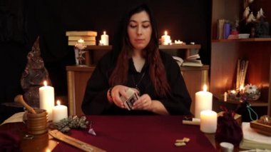 Bir cadı, siyah cüppeli falcıdır. Tarot kartları, eski rünler ve beyaz mumlar. Gizli, ezoterik, kehanet ve wicca kavramı. Mistik ve vintage arka plan.