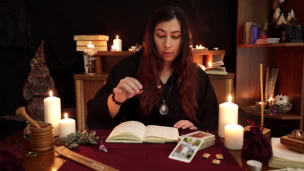 女巫是算命师 穿着黑色斗篷 拿着咒语书 有吸烟的香气棒和召唤精神 塔罗牌 蜡烛和黑色背景的流板 深奥和神化概念 — 图库视频影像