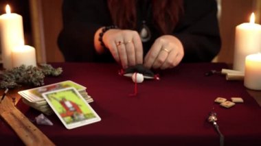 Bir cadı siyah manto kırmızı iplikleri ile vudu bebek tutun falcı olduğunu. Büyülü bir ritüel. Tarot kartları, masada beyaz mumlar. Gizli, ezoterik, kehanet ve Wicca kavramı. Mistik arka plan.