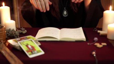 Bir cadı, siyah mantoda falcıdır. Tarot kartları, beyaz mumlar ve mistik arka plan üzerinde antik rünler. Gizli, ezoterik ve kehanet kavramı