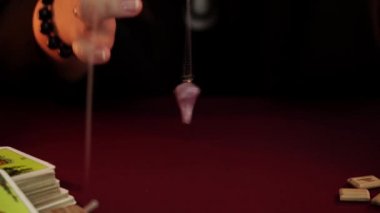 Bir cadı cüppe falcı kara büyü bir ayin gerçekleştirir. Sarkaç evet diyor. Büyülü bir ritüel. Tarot kartları, beyaz mumlar ve rünler. Gizli, ezoterik ve kehanet kavramı. Mistik arka plan.