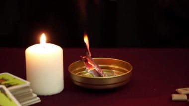 Büyü kağıt koyu bir mistik arka plan karşı beyaz mum yanında altın bir kase yakar ve yanar. Tarot kartları, taş üzerinde eski ahşap rünler. Gizli, ezoterik, kehanet ve wicca kavramı.