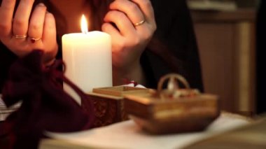 Cadı, yüzüklerle siyah mantolu bir falcı, beyaz bir mum üflüyor. Tarot kartları, ametist taşları, karanlık ve gizemli arka planda beyaz mumlar. Okült, esrarengiz, kehanet ve cadı kavramı.