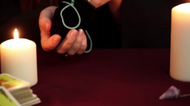 Cadı siyah mantolu bir falcı çantadan antik rünleri çıkartıyor. Tarot kartları, ametist taşları, karanlık ve gizemli arka planda beyaz mumlar. Okült, esrarengiz, kehanet ve cadı kavramı.