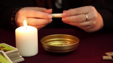 Cadı, siyah mantolu bir falcı. Sihir yakıp altın kaseye koyuyorlar. Tarot kartları, ametist taşları, karanlık ve gizemli arka planda beyaz mumlar. Okült, esrarengiz, kehanet ve cadı kavramı.