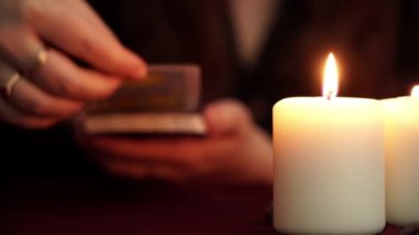 Bir cadı siyah manto tarot kartı göstermek falcı olduğunu. Masada beyaz mumlar var. Gizli, ezoterik, kehanet ve wicca kavramı. Çeviri: Ay.