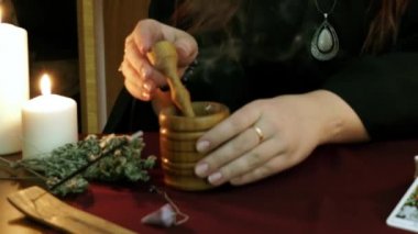 Bir cadı siyah manto lu falcı harç ezme ve havaneli kullanarak sallar pelin koymak. Büyülü bir ritüel. Tarot kartları, masada beyaz mumlar. Gizli, ezoterik, kehanet ve Wicca kavramı.