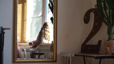 Leopar pantolon ve mor ayakkabı uzun sarı saçlı küçük bir kız aynadan bakıyor. Kız pencere nin üzerine tırmandı ve plastik pencereden dışarı baktı. Parlak güneş parlar.