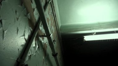 Yeşil boya çatladı ve eski bir sanayi fabrikasında soyulmuş kahverengi duvardan uzağa düştü. Eski paslı borular ve koyu siyah bir koridorda beton tavana asılı uzun bir floresan lamba.