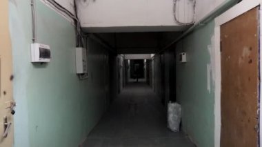 Eski ahşap ve çelik kapılar çok yeşil soyulmuş duvarları ile koyu uzun koridor. Duvarlarda kablolar ve elektrik kutuları var. Önünde yürüyen bir adamın silueti. Beton tavanda floresan lamba.