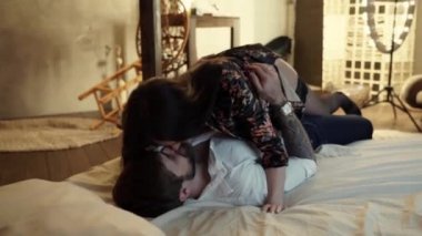Bir ipek bornoz uzun siyah saçlı seksi bir kadın üstüne yatıyor ve sıcak ışık ile yatak odasında saat ve dövme ile beyaz gömlek beyaz sakallı adam hakim. Bej yatakta yatan çift.