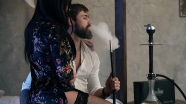 Düz uzun siyah saçlı seksi kız ipek sabahlık taş duvarlar ile bir yatak odasında beyaz düğmesiz gömlek kısa kahverengi saçlı sakallı kafkas bir adam sarılma. Çift sigara nargile.
