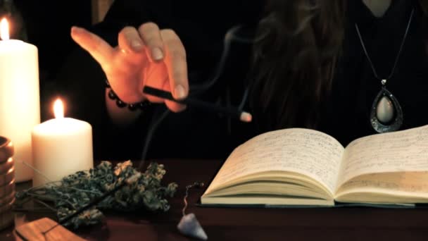 女巫是算命师 穿着黑色斗篷 拿着咒语书 有吸烟的香气棒和召唤精神 塔罗牌 蜡烛和黑色背景的流板 深奥和神化概念 — 图库视频影像