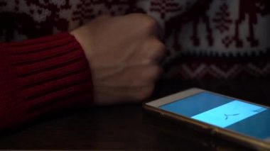 Kırmızı bir kazak ve masada dahil ekran ile beyaz bir telefon izleri ve damarlarla genç bir adamın elini yakın çekim. Bir kuş ekranda uçar. Bir adam düğmesi bulamıyor ve ses aşağı çevirmek.