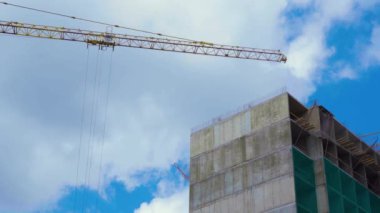 Güzel bulutlu mavi gökyüzü bir arka plan üzerinde beton Sanayi binası yakınında kendi kendine ereksiyon yüksek kule vinç Düşük görünümü. Büyük konut binaları inşa etmek için hangi şantiye.