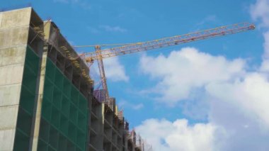 Güzel bulutlu mavi gökyüzü bir arka plan üzerinde beton Sanayi binası yakınında kendi kendine ereksiyon yüksek kule vinç Düşük görünümü. Yüksek katlı binaların inşa edilebilecek şantiye.