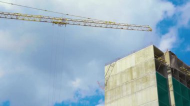 Güneş, bulutlu mavi gökyüzünün arka planında hareketli vinç ile yüksek kule vinç yakınında kendi kendine ereksiyon beton Endüstriyel bina aydınlatır. Konut inşası için şantiye.