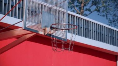 Turuncu ve siyah top bir basketbol sahası üzerinde uçar ve güneşli yaz gününde metal zincir net ile çember üzerinden ağaç arka plan üzerinde yakın düşmek. Modern kentsel kırmızı oyun alanı kavramı.