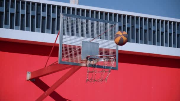 橙色和黑色球飞过篮球场 在阳光明媚的夏日用金属链网从篮子里掉下来 现代城市红色运动场的概念 得分赢点 — 图库视频影像