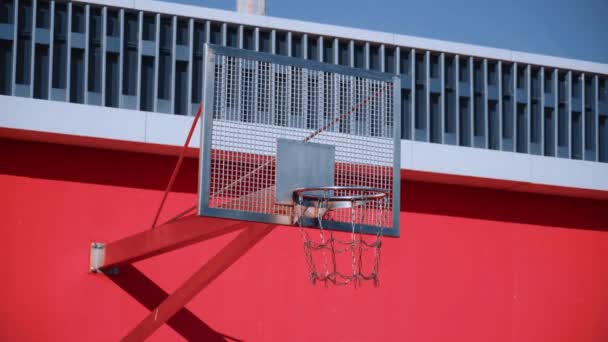 在阳光明媚的夏日 阳光明媚的夏日 阳光明媚的蓝天 篮子的金属链网在美丽的现代红色篮球场上摆动 学校或公园城市红色运动场的概念 网格背板 — 图库视频影像