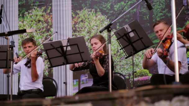 野外でストリートミュージシャンのアンサンブル 黒いスーツを着た女性と男性は 日没時に木製のバイオリンでクラシック音楽を演奏します 公園で演奏する交響楽団ヴィオラと第二ヴァイオリンセクション — ストック動画
