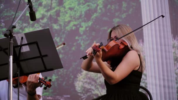 露天街头音乐家的合奏 身着黑色礼服的金发美女在日落时分在美丽的木小提琴上演奏古典音乐 交响乐团第二小提琴部分在公园演出 — 图库视频影像