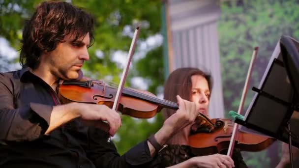 英俊的黑发男子在黑色衬衫和女人在礼服发挥古典乐器户外 交响乐团第一小提琴部分在公园演出 露天街头音乐家的合奏 — 图库视频影像