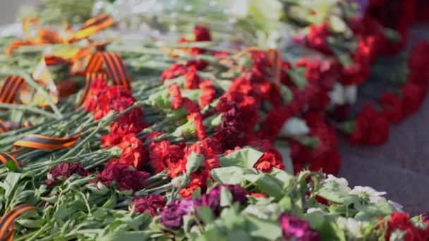 未知の兵士の墓の永遠の炎の記念碑に聖ジョージリボンと赤と白の葬儀の花 第二次世界大戦での勝利の象徴と何百万人のソ連の犠牲者の記憶 — ストック動画