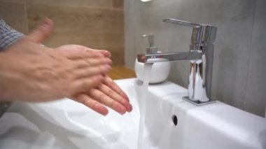 Coronavirus salgını önleme. İşçi adam ellerini musluktan gelen sabunla iyice yıkar, parmaklarını sıkça ovar, yıkar, el dezenfektanı ya da dezenfektan kullanır. Musluğu kapatır.