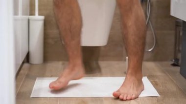 Zayıf adam banyoda hızlı koşar, beyaz halıya çıkar, klozetin üzerine oturur, gri pantolonunu çıkarır, yerden tuvalet kağıdını kapar. İshal krizi. Sindirim sorunları. Gıda zehirlenmesi. İç görünüm.