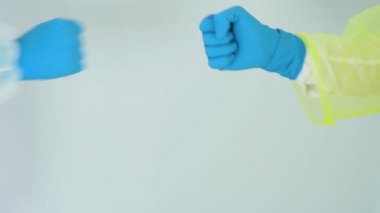 Koruyucu takım elbiseli iki doktor, mavi lastik eldiven beyaz arka planda yumruk tokuşturuyor. İnsanlar çalışmada bağlılık ve başarı gösterirler. Kilitleme döneminde koruma kavramı. Boşluğu kopyala.