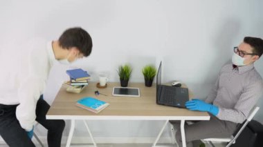 Bir adam gelip iş bulur, açık dizüstü bilgisayar, kitaplar ve tabletle beyaz duvarın arkasına oturur. Ofis odasında konuşan iki genç adam. İnsanlar tıbbi maske, mavi lastik eldiven ve gömlek takıyor. İç görünüm.