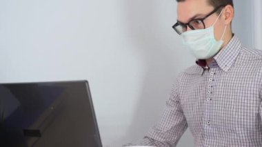 Genç yakışıklı adam siyah gözlük takıyor, tek kullanımlık tıbbi turkuaz maske takıyor, beyaz lateks eldivenler giyiyor, klasik gri gömlek konuşuyor, iletişim kuruyor, dizüstü bilgisayardan canlı yayında konuşuyor. İşçi çocuk, evde kal.