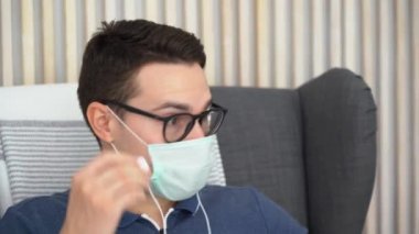 Genç esmer, beyaz, yakışıklı bir adamın yakın portresi. Hastalıklı bir adam koruyucu turkuaz maske takıyor, siyah gözlükler takıyor, kulaklık takıyor, müzik dinliyor, rahatlıyor, eğleniyor..