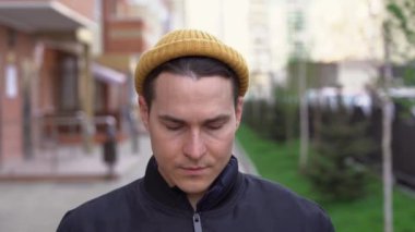 Genç ve yakışıklı bir esmer adam sarı kış şapkası, ceket giyiyor. Beyaz harfli siyah maske takıyor. Bulanık şehir sokaklarının arka planında Covid-19 yazıyor. Konsepti kilitle.