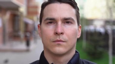 Kısa kahverengi saçlı, beyaz Covid-19 yazılı siyah yüz maskesi takan yakışıklı, beyaz tenli esmer adam. Adam bulanık arkaplanda kendine güvenen bir şekilde kameraya bakıyor. Dış görünüm.