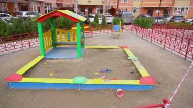 Pandemik karantina döneminde terk edilmiş, unutulmuş çocukların oyun parkı. Renkli oyuncaklar ve kovalar evlerin arasındaki kum havuzunda yatıyor. Boşluk. Kırmızı uyarı barikatı girişi kapatıyor. Salgın zamanı