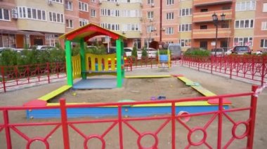 Terk edilmiş çocuk oyuncaklarıyla dolu oyun parkı kırmızı çitlerle çevrili ve girişi kapalı park halindeki arabaların arka planında uyarı bandı ile kapatılmış, yüksek konutlu bina. Hastalıktan salgın zamanı.
