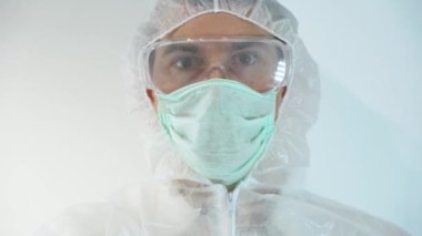 Erkek bilim adamı beyaz koruyucu elbise giyer, tek kullanımlık lastik eldiven giyer, virüslerle çalışır, şişeyi elinde tutar, COVID 19 için negatif kan testi gösterir. Analiz et, enfeksiyon kapmadığını, hasta olmadığını bil.