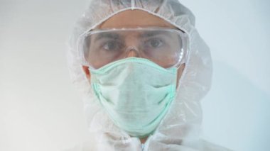 Beyaz hastane geçmişine izole edilmiş bir bilim adamı portresi. Bulaşıcı hastalıklar uzmanı koruyucu giysi giyer, kafasına başlık geçirir, maske takar, enfekte olmuş kanla test tüpünü inceler.