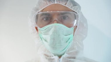 Sağlık ekibi koruyucu kıyafet giyer, beyaz hastane geçmişinde yeni bir aşı kullandıktan sonra eldivenli el emniyetli kan örneğini test tüpünün önünde tutar. Hastalık için negatif sonuç. Bilim adamı