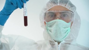 Kendine güvenen bilim adamı erkek koruyucu giysi, yüz maskesi, lastik eldiven giyer, elinde tutar, yeni deneysel aşı kullandıktan sonra kovid 19 negatif kan test tüpüne bakar. İnsanlar için ilaç yaptım..